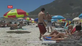 People resting on beach chairs under umbrellas 2 guys playing tennis