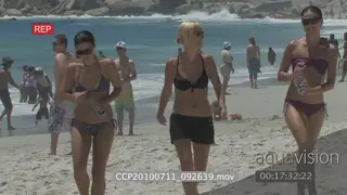 Model ladies in bikini's walking along beach people in BG playing beach games