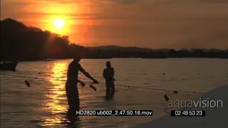 Silhouette shot of Local young men pulling fishing nets out of river orange sunset in BG